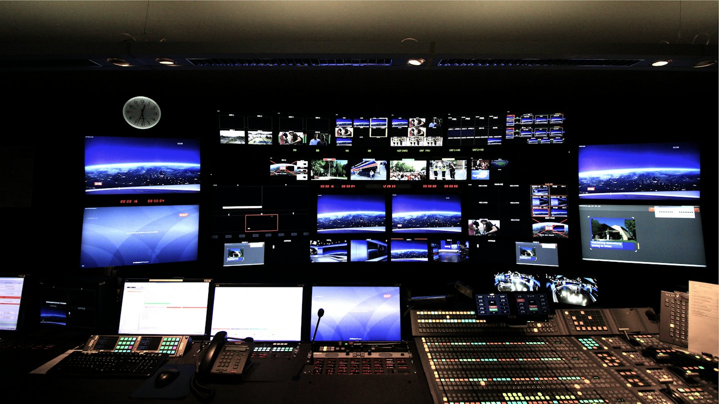 Sala de control de transmisiones con monitores brillantes y paneles de control.