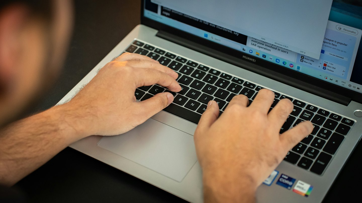 Una persona escribe en un portátil que muestra información y titulares.